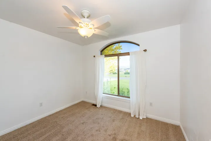 Room featuring a large arched window with a green outdoor landscape, neutral-toned carpeting, white baseboards, and a ceiling fan with integrated lighting