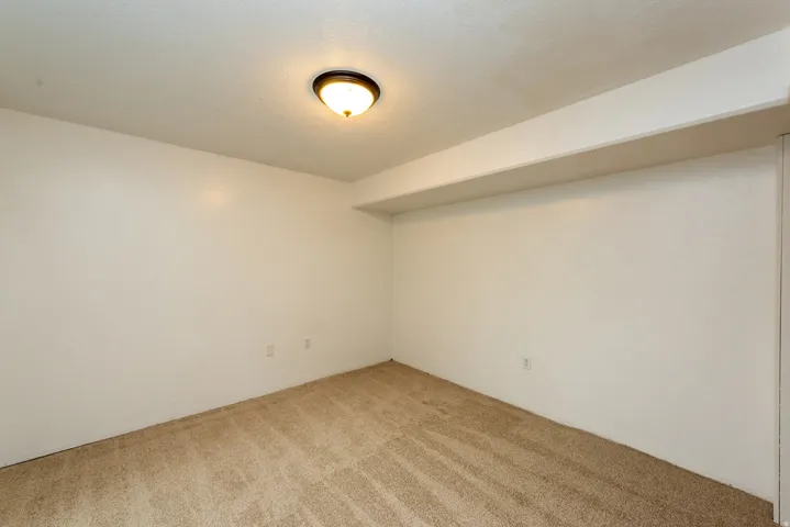 Carpeted room featuring a ceiling-mounted light fixture, white walls, and a visible ceiling beam