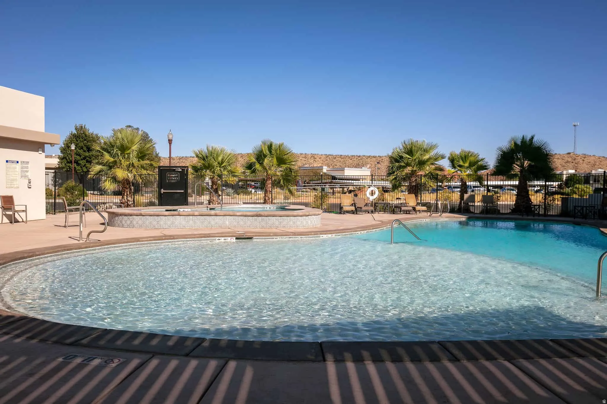 Curved swimming pool with an integrated spa, surrounded by concrete decking