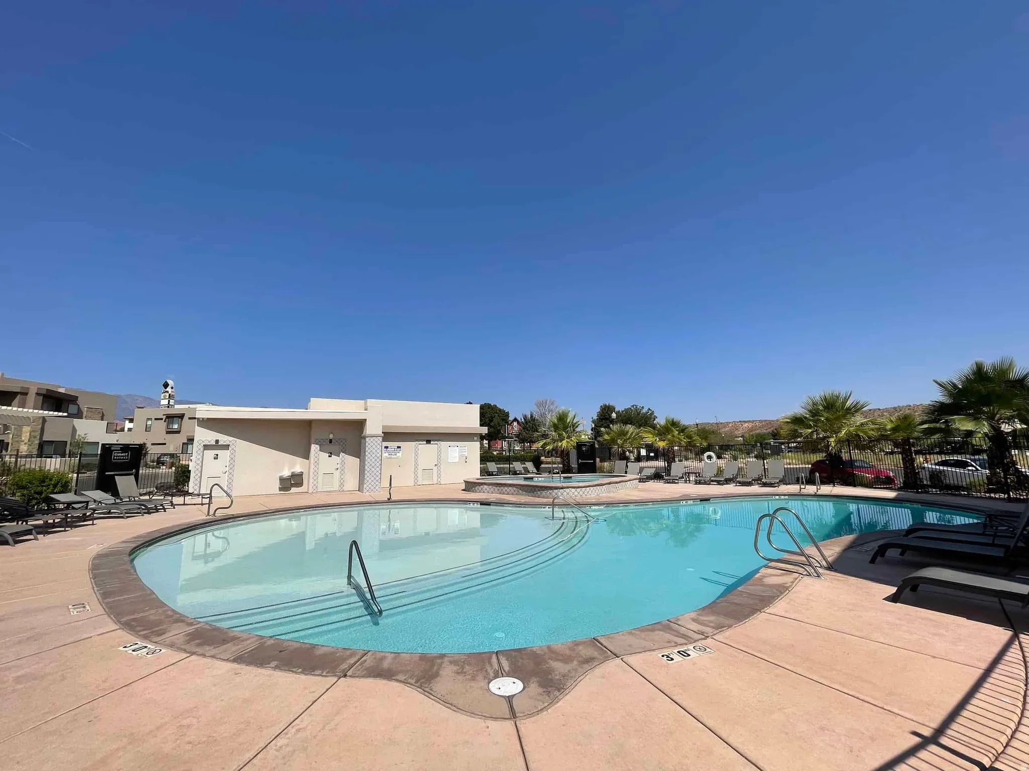 Resort-style pool area featuring a large swimming pool with gradual entry steps, an integrated spa, and expansive concrete decking