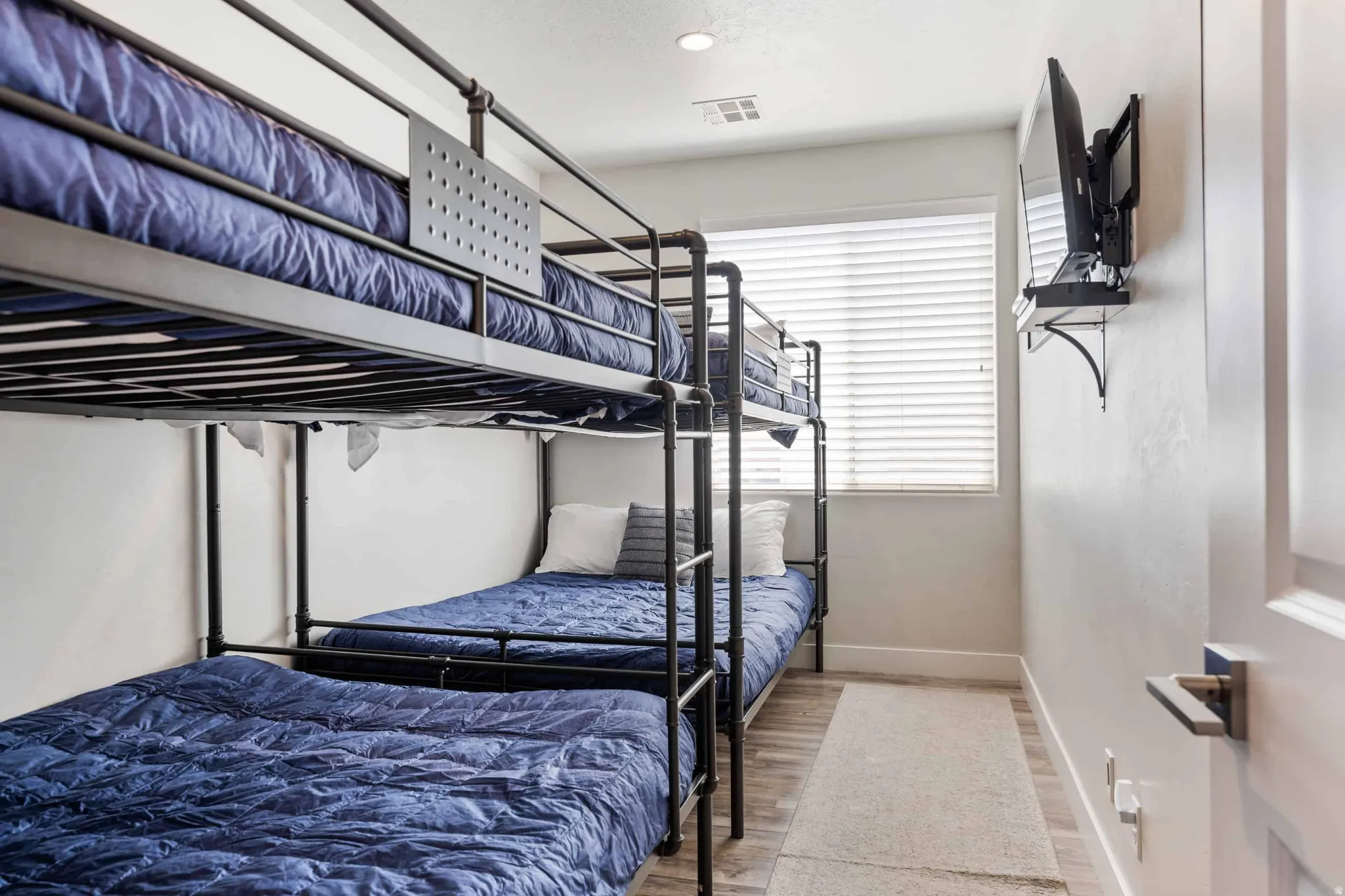 Room featuring a metal triple bunk bed frame, a single pane window with horizontal blinds, and recessed lighting
