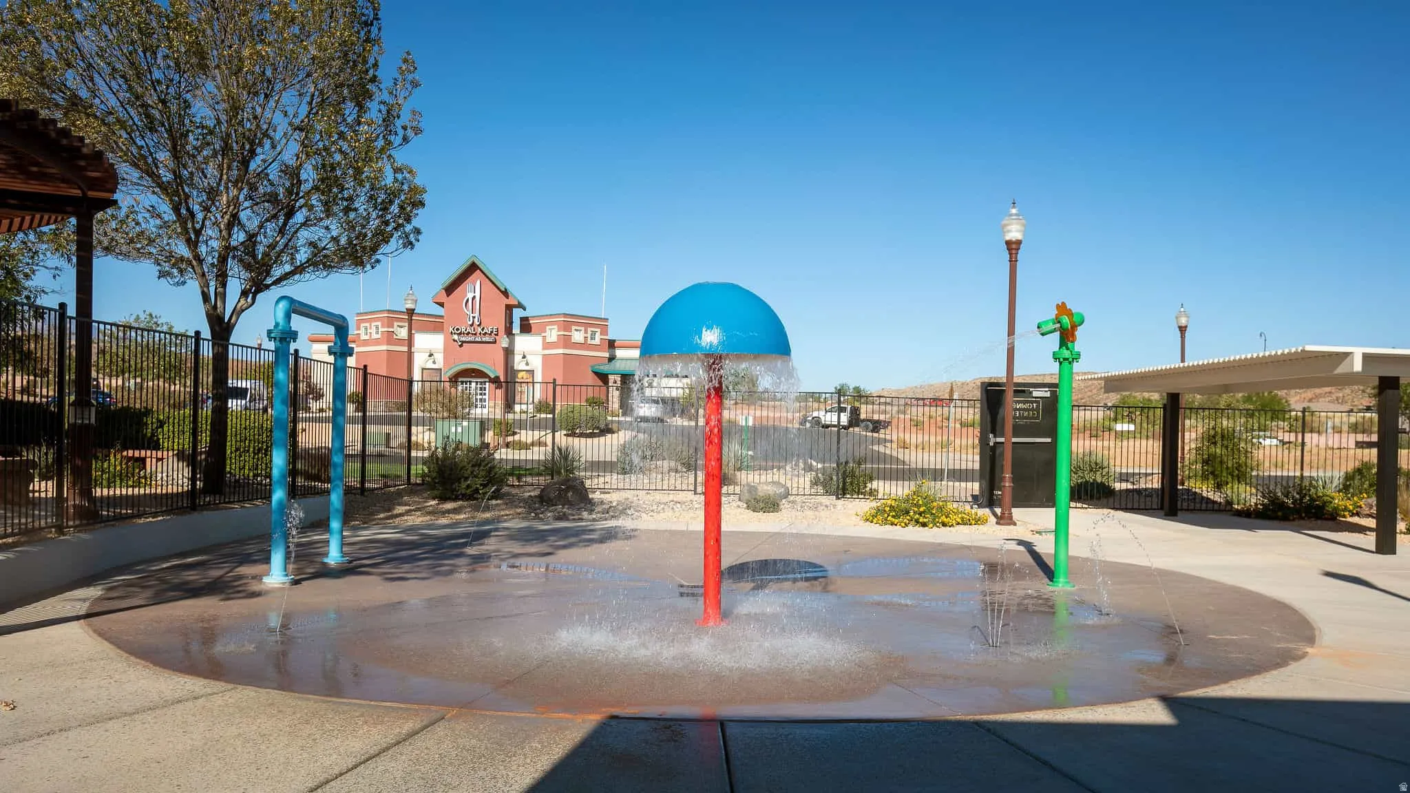 Splash pad featuring multiple water features, concrete surfacing, and a nearby pergola