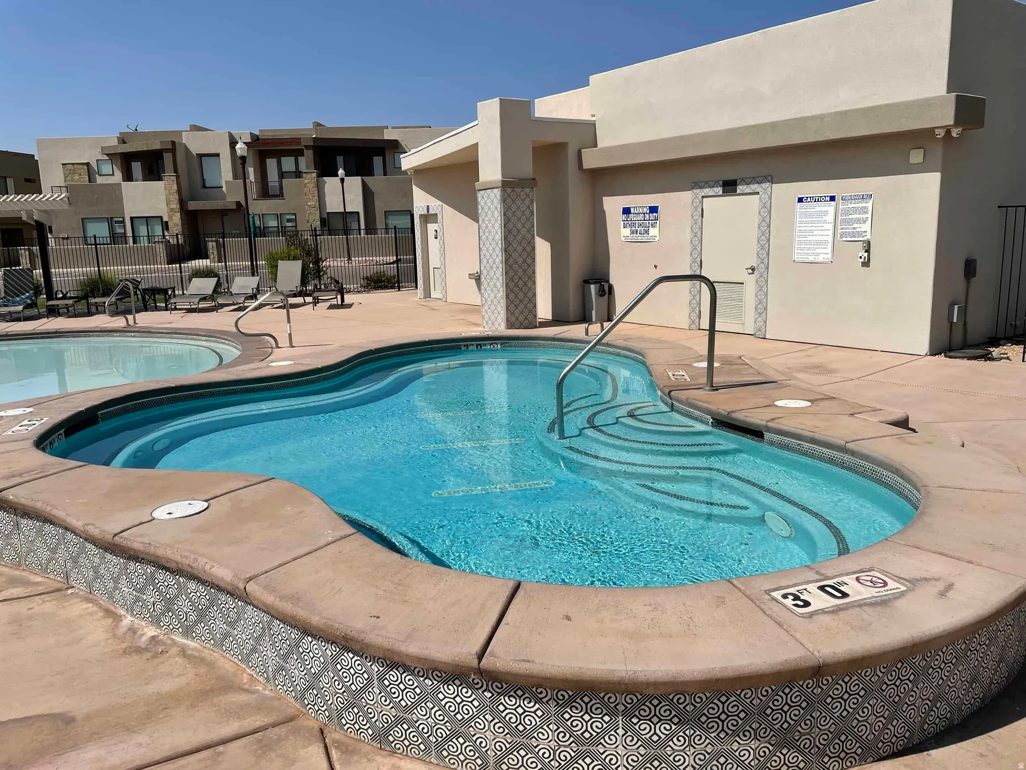 Resort-style pool area featuring a kidney-shaped pool with integrated steps, a separate circular pool, and a concrete deck with decorative tile accents