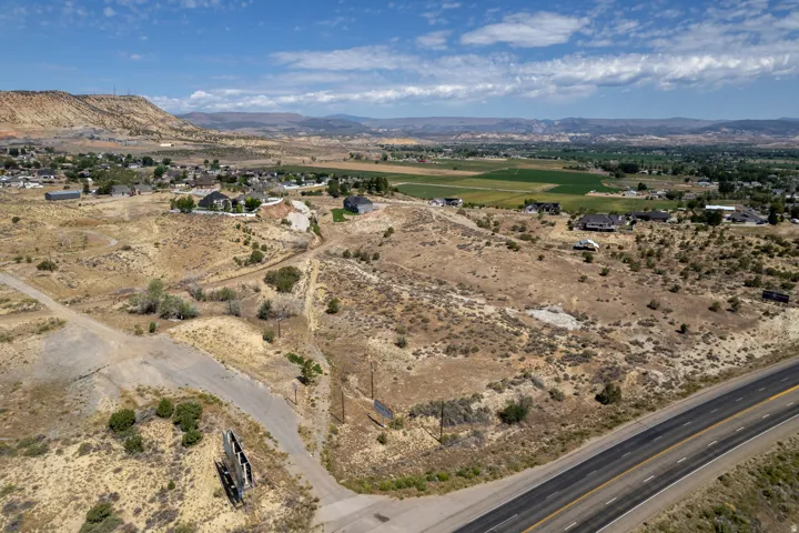 Expansive undeveloped land featuring a paved road frontage and distant residential structures