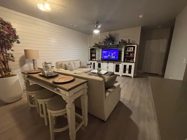 Living area featuring wood-finish flooring, a ceiling fan, and a shiplap accent wall