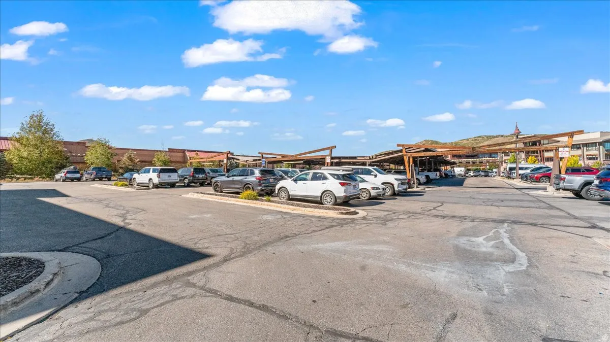 Paved parking lot with designated spaces, featuring covered parking structures with slatted roofs