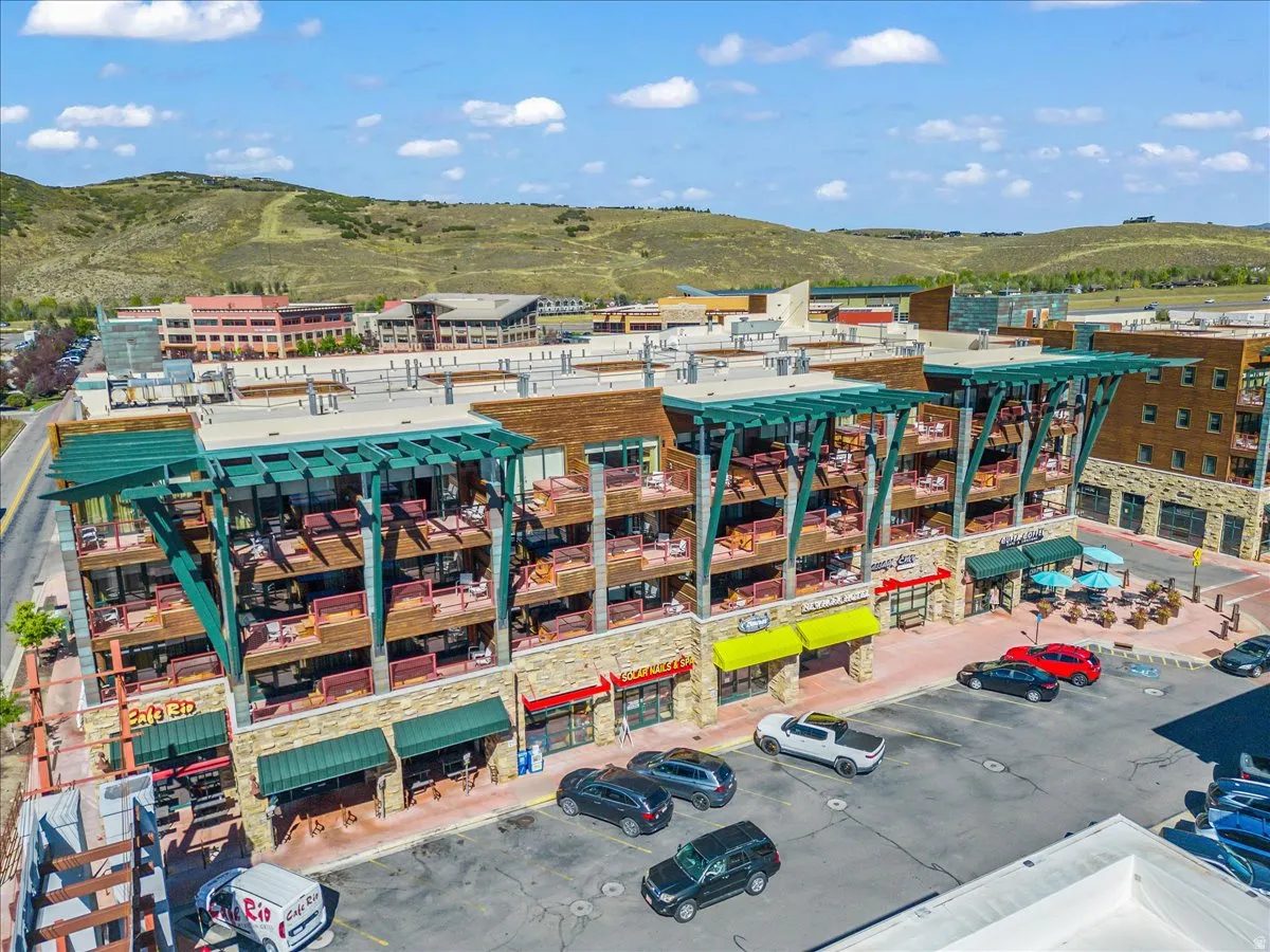 Multi-story commercial building featuring multiple retail spaces, upper-level residential units with private balconies, stone and brick facade, and prominent green architectural accents