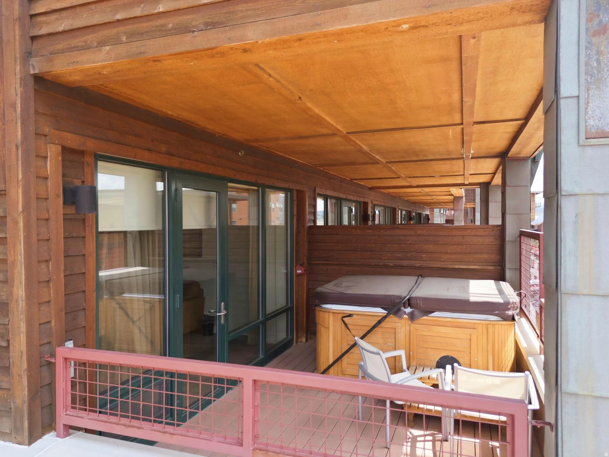 Covered balcony featuring a built-in hot tub, wood plank decking, and a metal grid railing