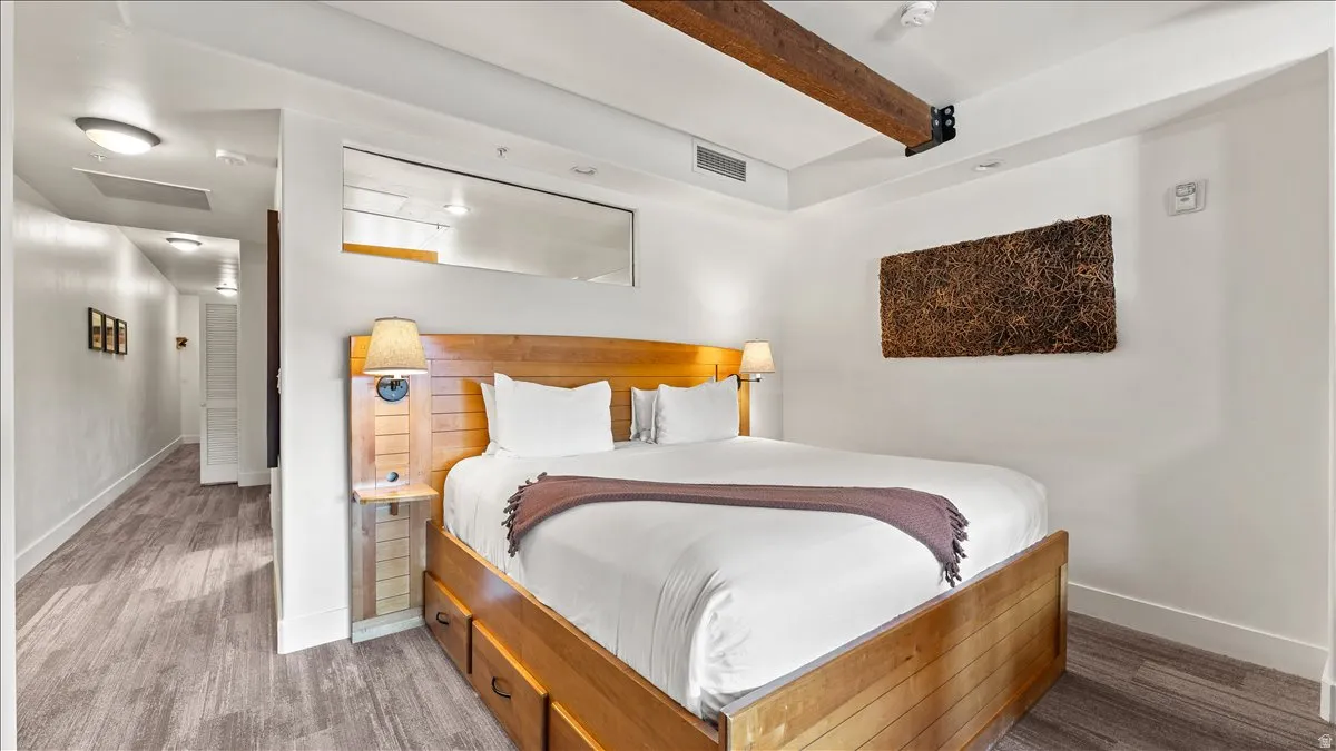 Bedroom featuring wood-finish flooring, a wood-frame bed with integrated drawers, and a wood-paneled headboard with attached sconces