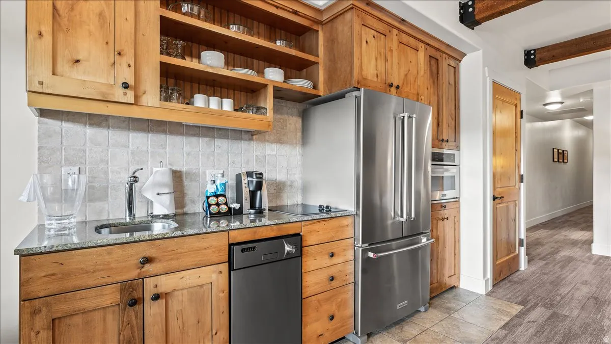 Kitchenette featuring wood cabinetry, stainless steel appliances, a built-in microwave, a tiled backsplash, and granite countertops