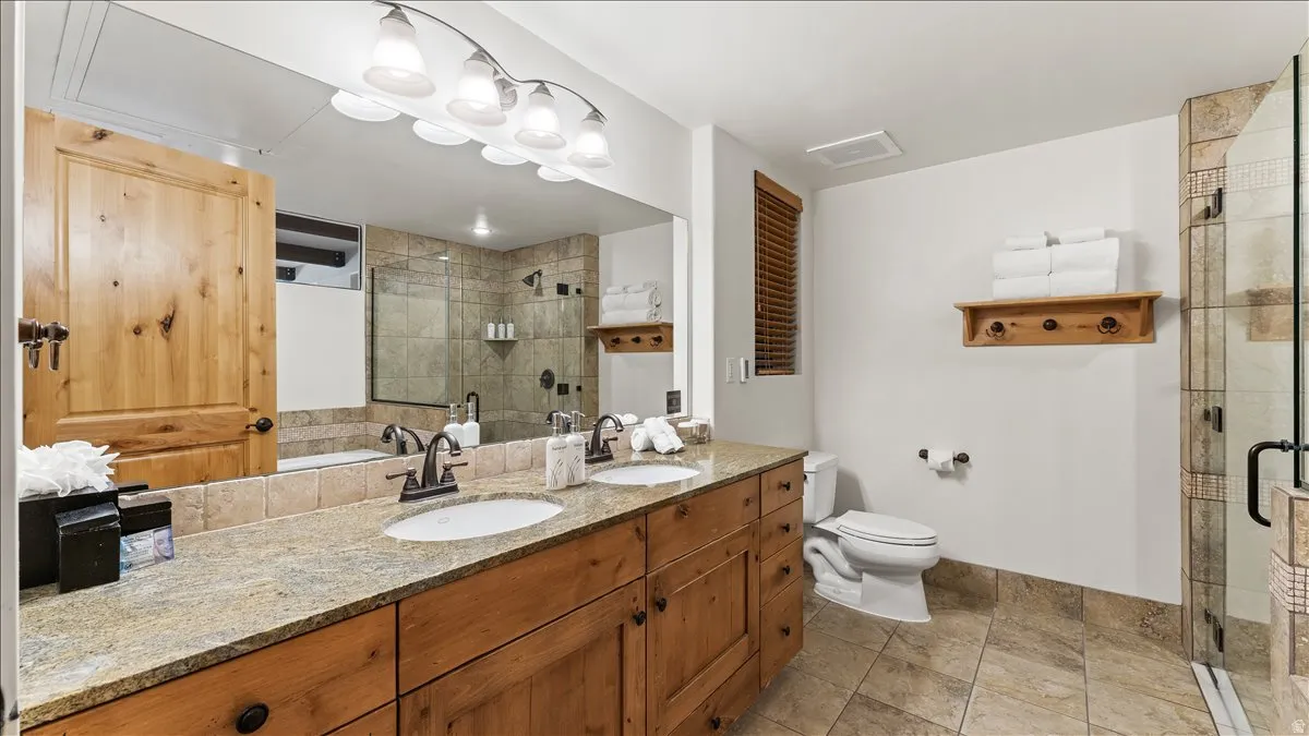 Bathroom featuring a double vanity with granite-style countertop, wood cabinetry, and a full-width mirror