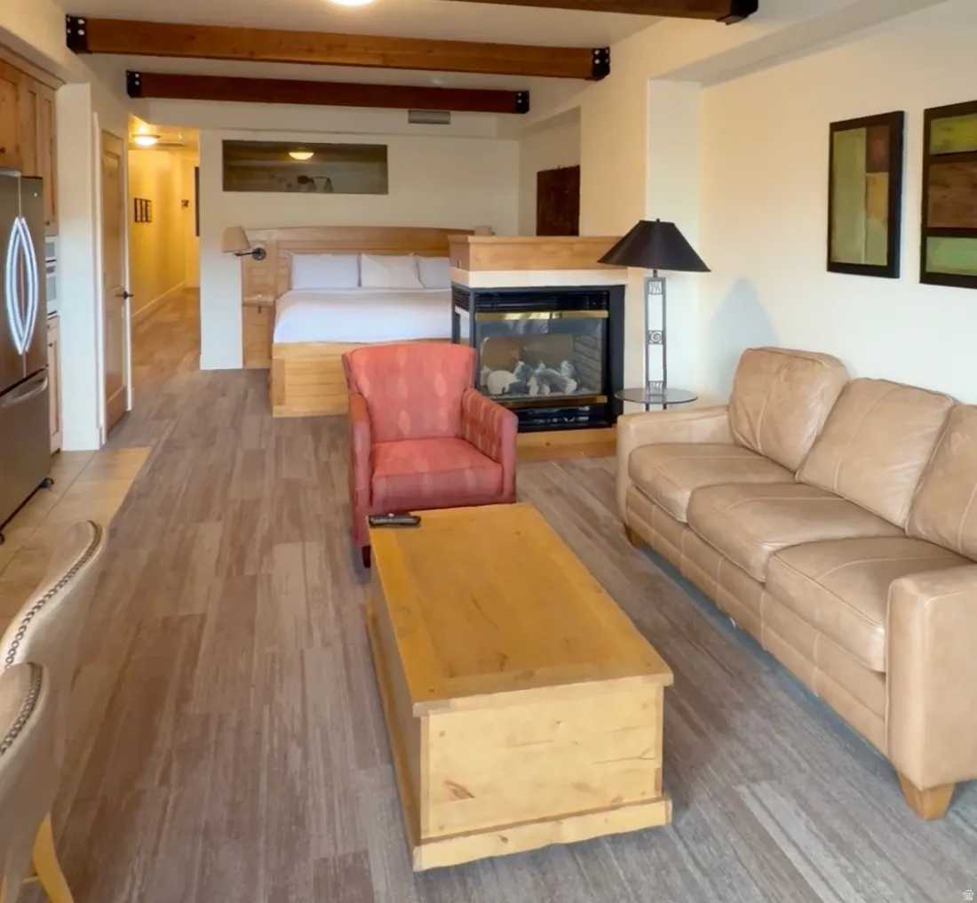 Open-concept living space with exposed wood beams, wood-finish flooring, a built-in fireplace, and integrated kitchen cabinetry