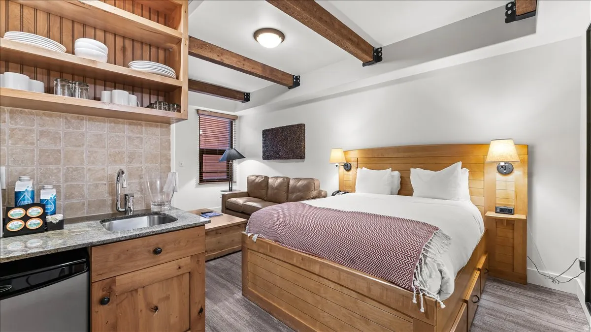 Open concept room featuring a wood-finish bed frame, built-in shelving, and exposed ceiling beams