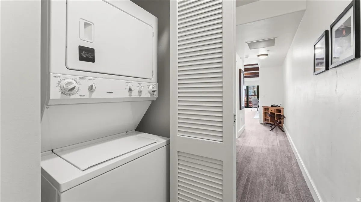 Dedicated laundry closet featuring a stacked washer and dryer, louvered bi-fold door, and wood-finish flooring extending into the hallway