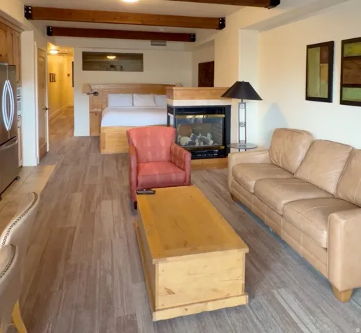 Open-concept living space with exposed wood beams, wood-finish flooring, a built-in fireplace, and integrated kitchen cabinetry