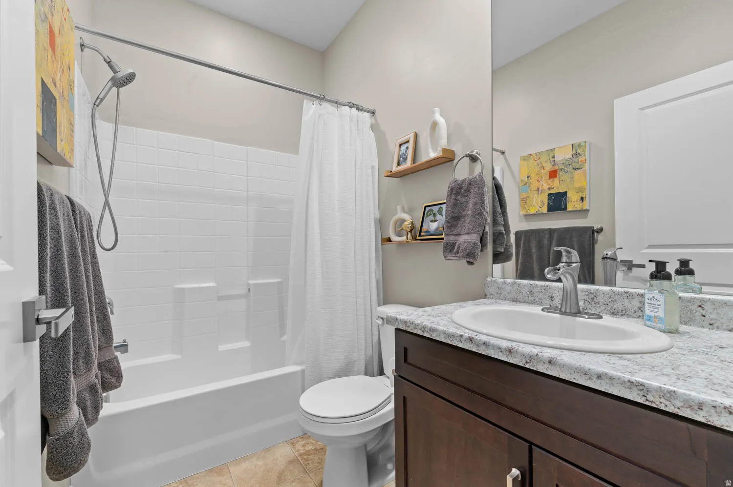 Bathroom featuring a tub/shower combination with white subway tile surround, dark wood-finish vanity with a light speckled countertop, and tiled flooring