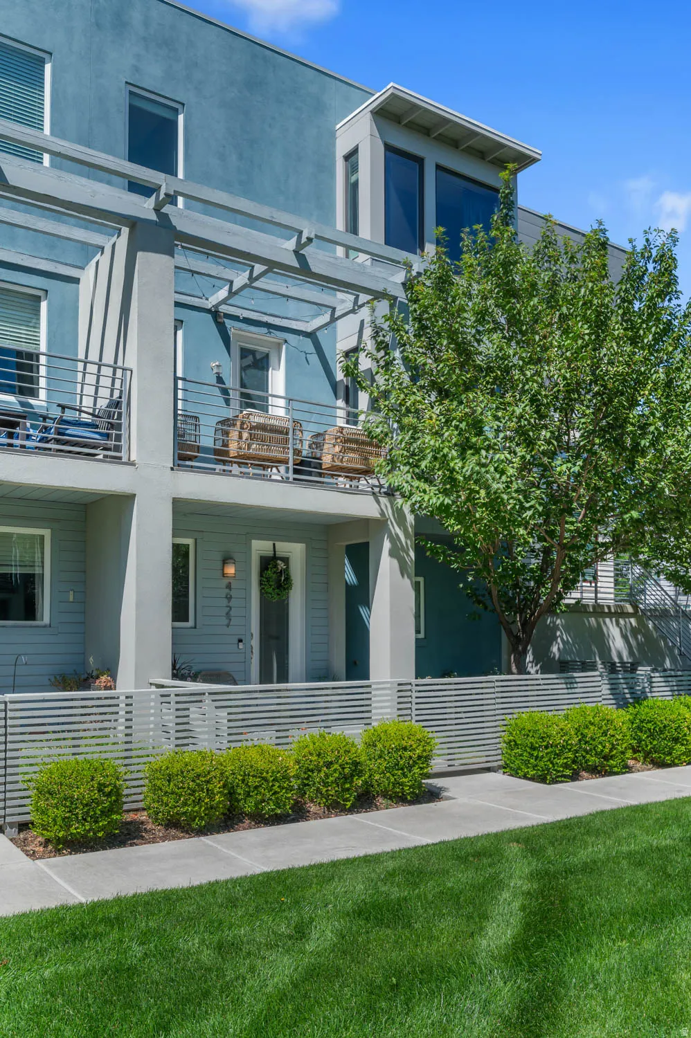 Modern multi-level facade featuring a covered entry, a second-story balcony with metal railings and a pergola, and a third-story architectural window box