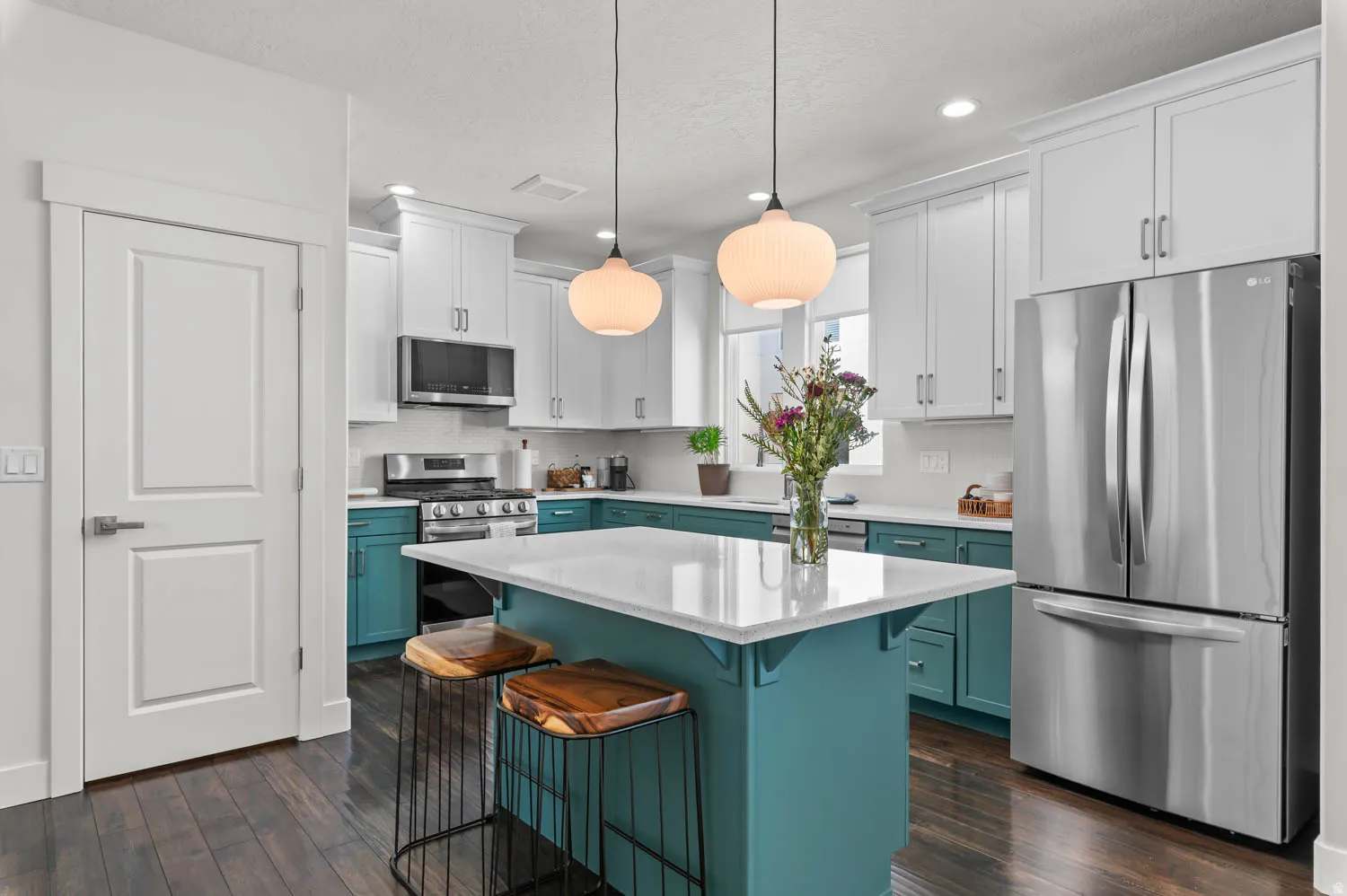Kitchen featuring a central island with white countertop, two-tone cabinetry, stainless steel appliances, and wood-finish flooring
