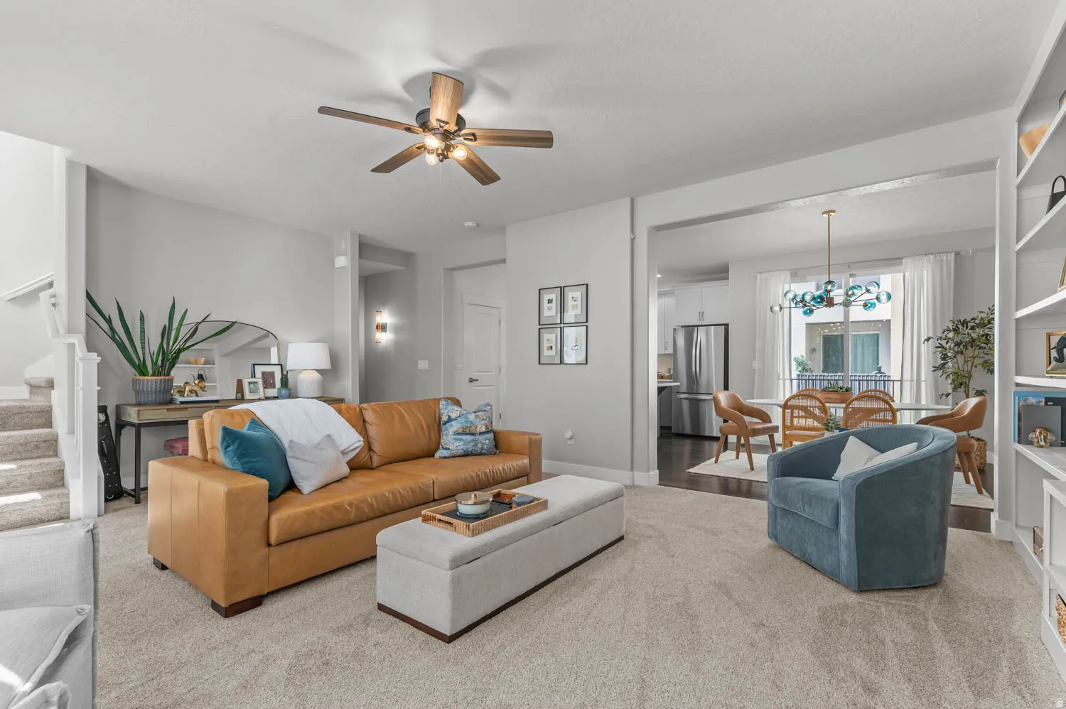 Spacious living area featuring neutral carpeting, a ceiling fan, and an open doorway to a dining space