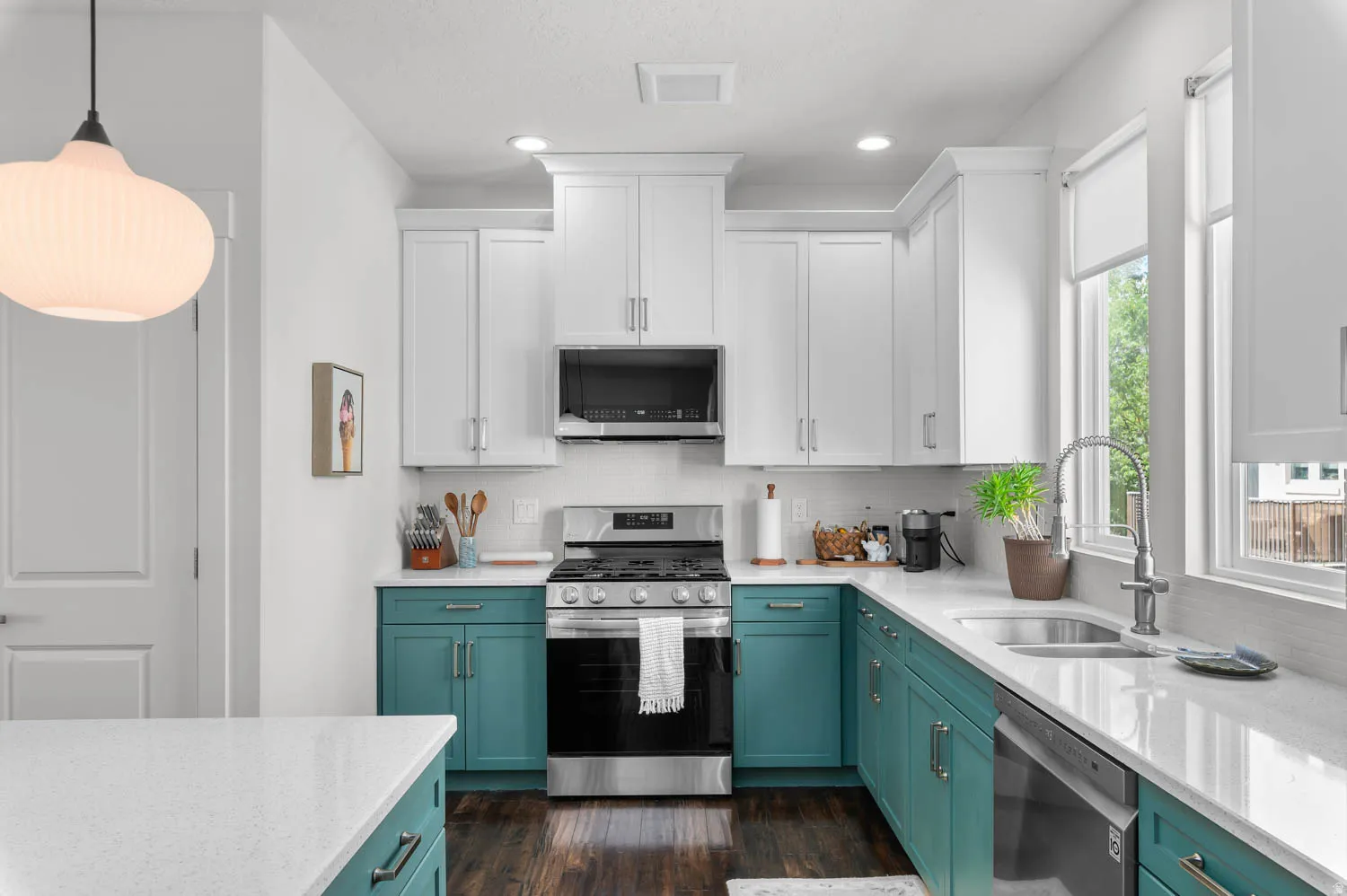 Modern kitchen featuring two-tone cabinetry with white upper and teal lower cabinets, stainless steel appliances, and wood-finish flooring