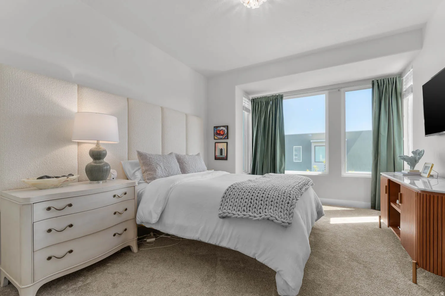 Carpeted room featuring a large bay window, light-toned upholstered wall paneling, a ceiling-mounted light fixture, and white painted walls