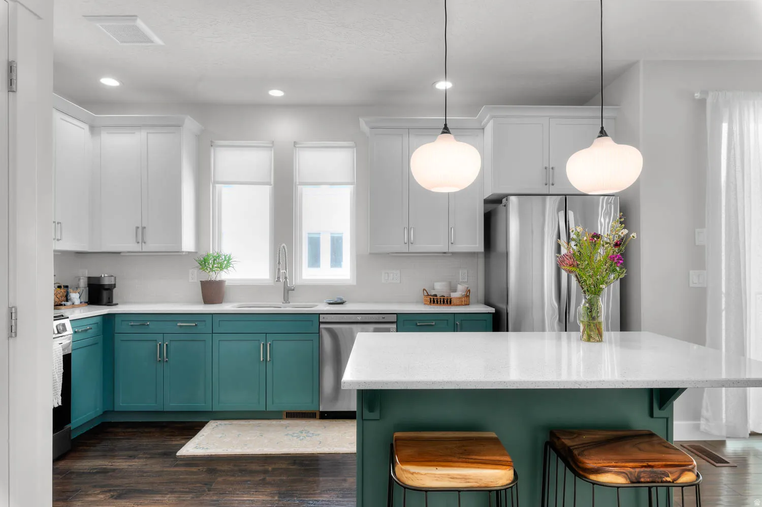 Kitchen featuring two-tone cabinetry with white upper and teal lower cabinets, a central island with countertop seating, stainless steel appliances, and dark wood-finish flooring