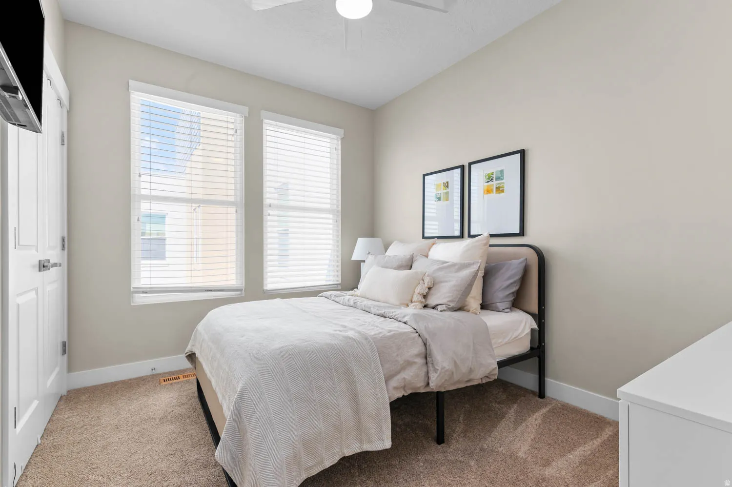 Neutral-toned room featuring a light beige carpet, two windows with blinds, a white ceiling fan, and white baseboards