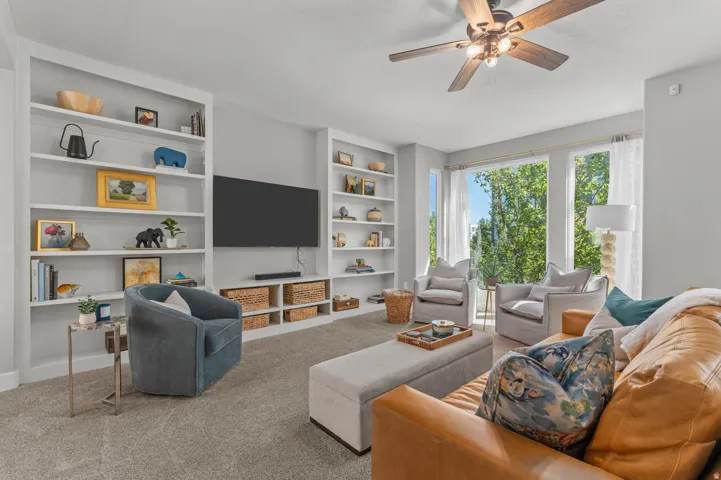 Living area featuring extensive built-in shelving, a wood-finish ceiling fan, and large windows