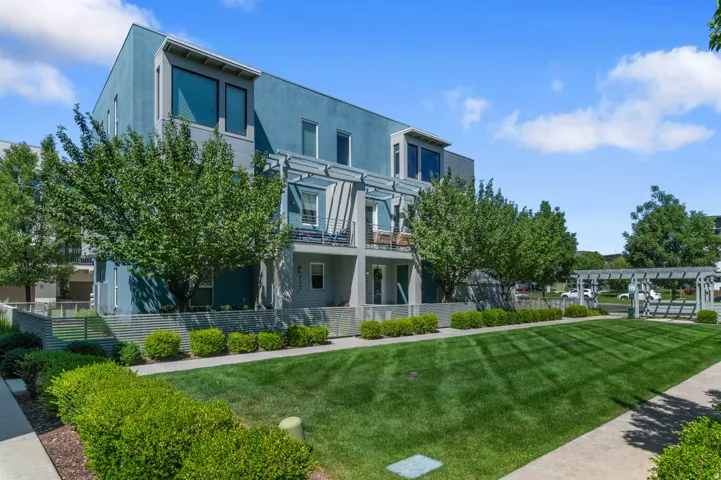 Modern multi-story building featuring a blue and gray facade, multiple balconies with metal railings, large windows, and a structured pergola