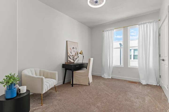 Carpeted room featuring multiple windows with white window treatments, white painted walls, and a ceiling-mounted light fixture
