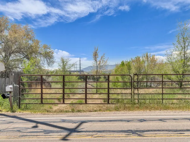 Gated property entrance featuring metal fencing, a mailbox, and a paved road frontage