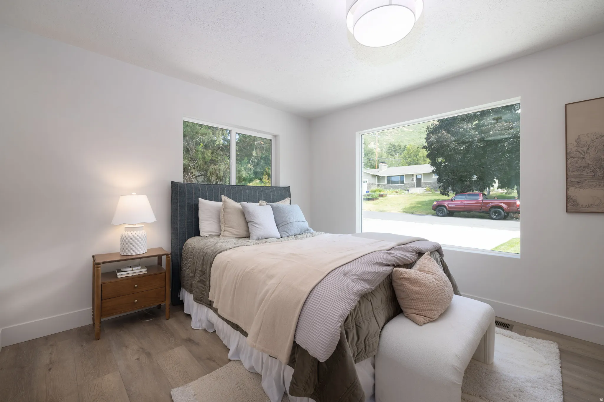 Bright room featuring a large picture window, wood-finish flooring, white baseboards, and a semi-flush mount ceiling light