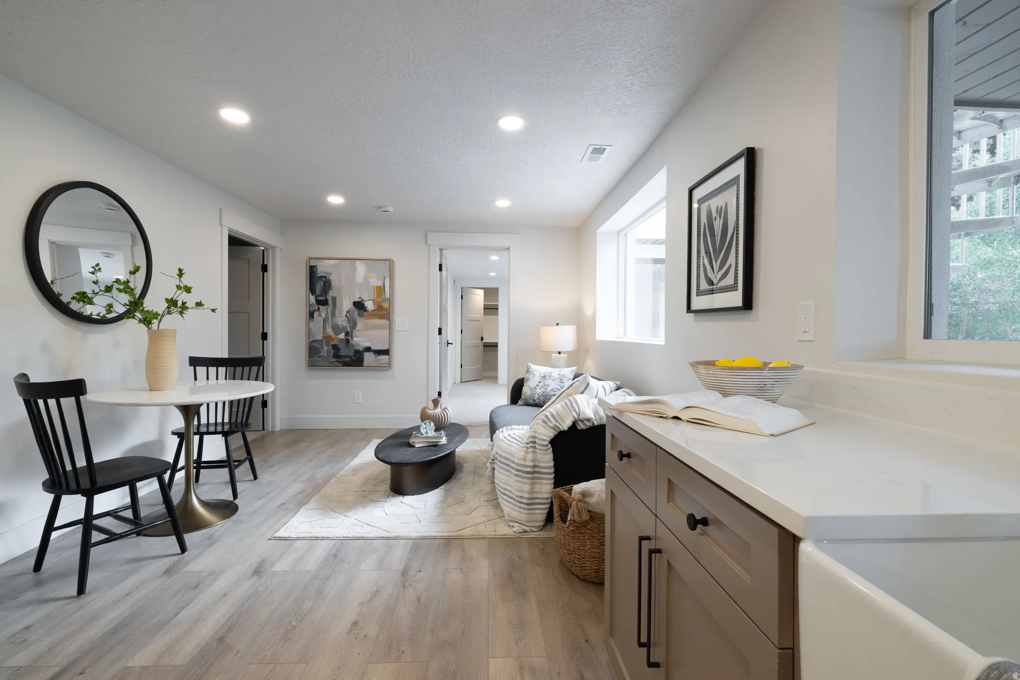 Open-concept living space featuring light wood-finish flooring, recessed lighting, and a white countertop with an integrated farmhouse-style sink