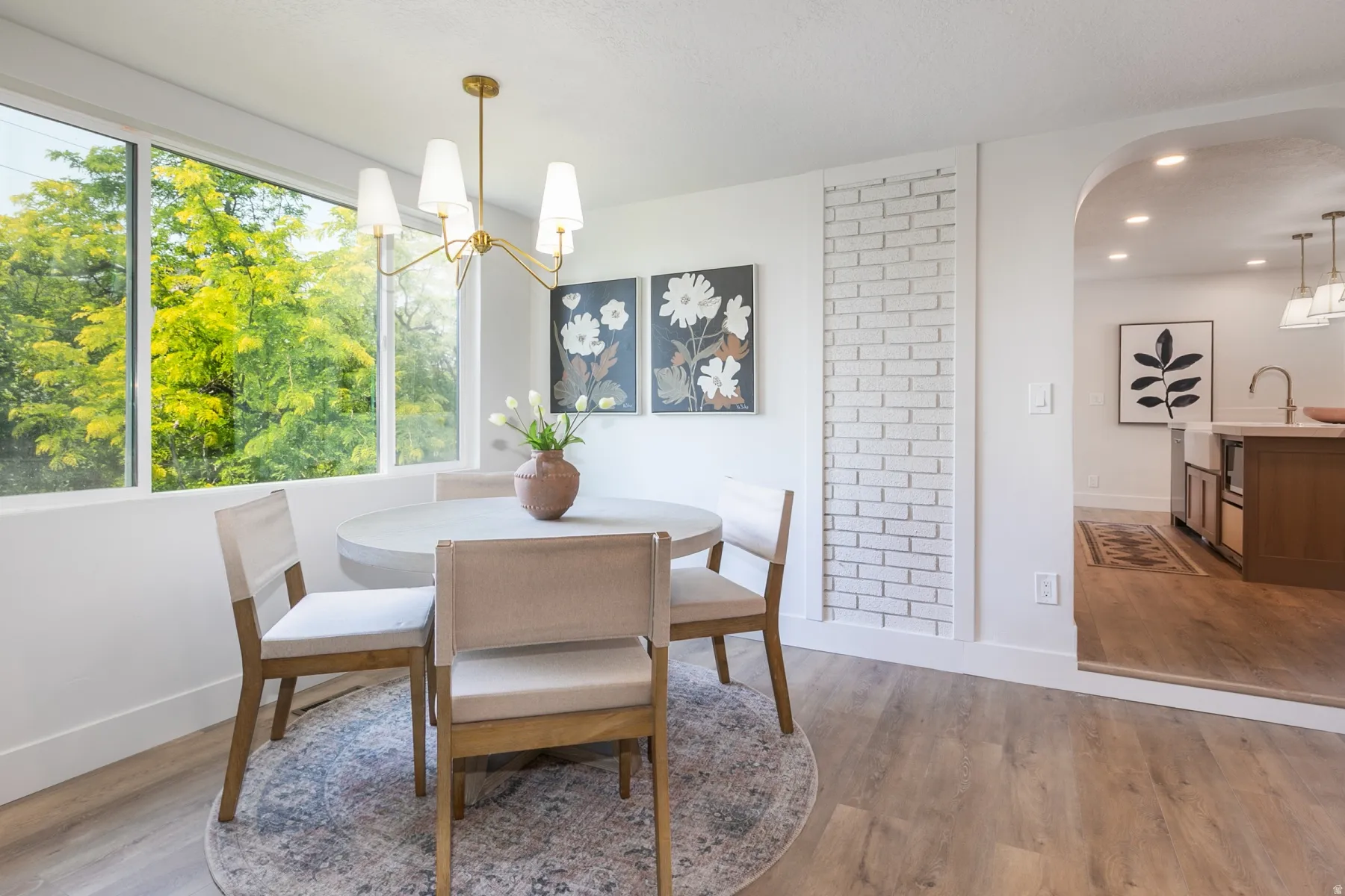 Dining area featuring a contemporary gold-finish chandelier, large picture windows, wood-finish flooring, a decorative brick accent wall, and an arched entry