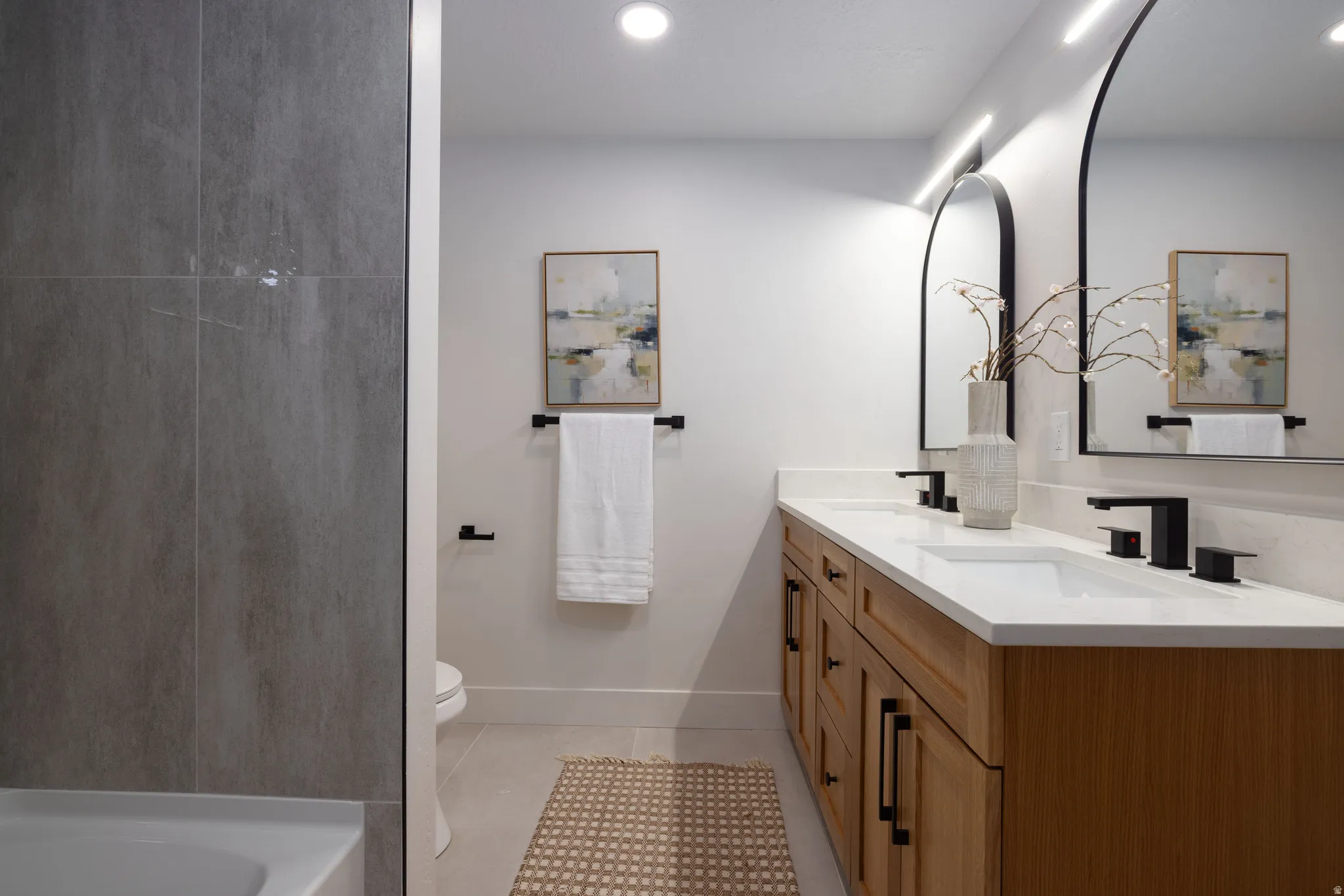 Dual vanity with wood-finish cabinetry, white countertops, and matte black fixtures