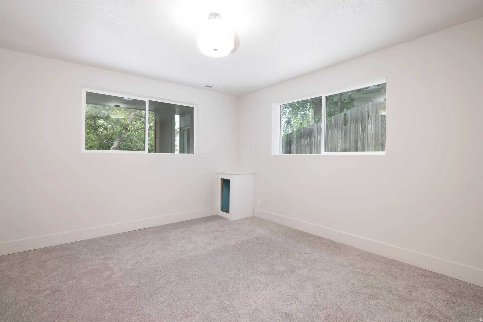 Neutral tone wall paint with a textured ceiling finish, two windows, wall-to-wall carpeting, and a built-in wall niche