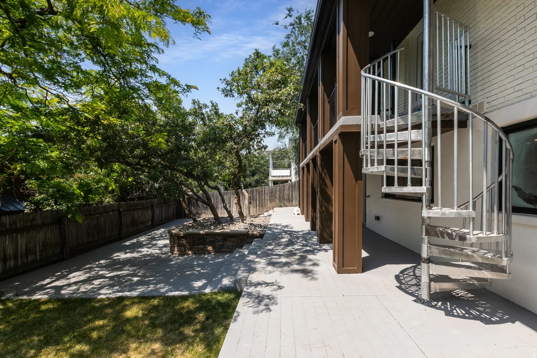 Outdoor patio featuring a spiral staircase, established trees, and a stone-built planter