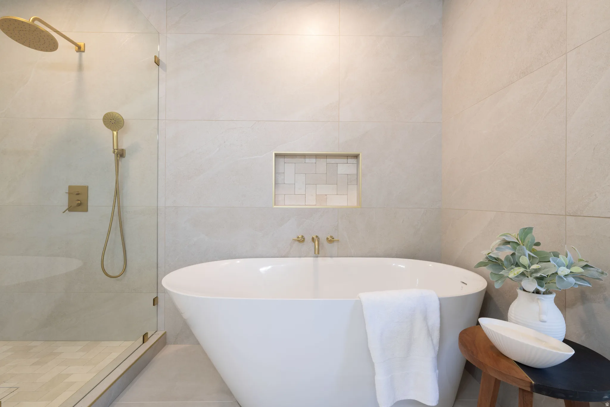 Modern bathroom featuring a freestanding soaking tub, glass-enclosed shower with gold-tone fixtures, and a recessed shower niche with decorative tile