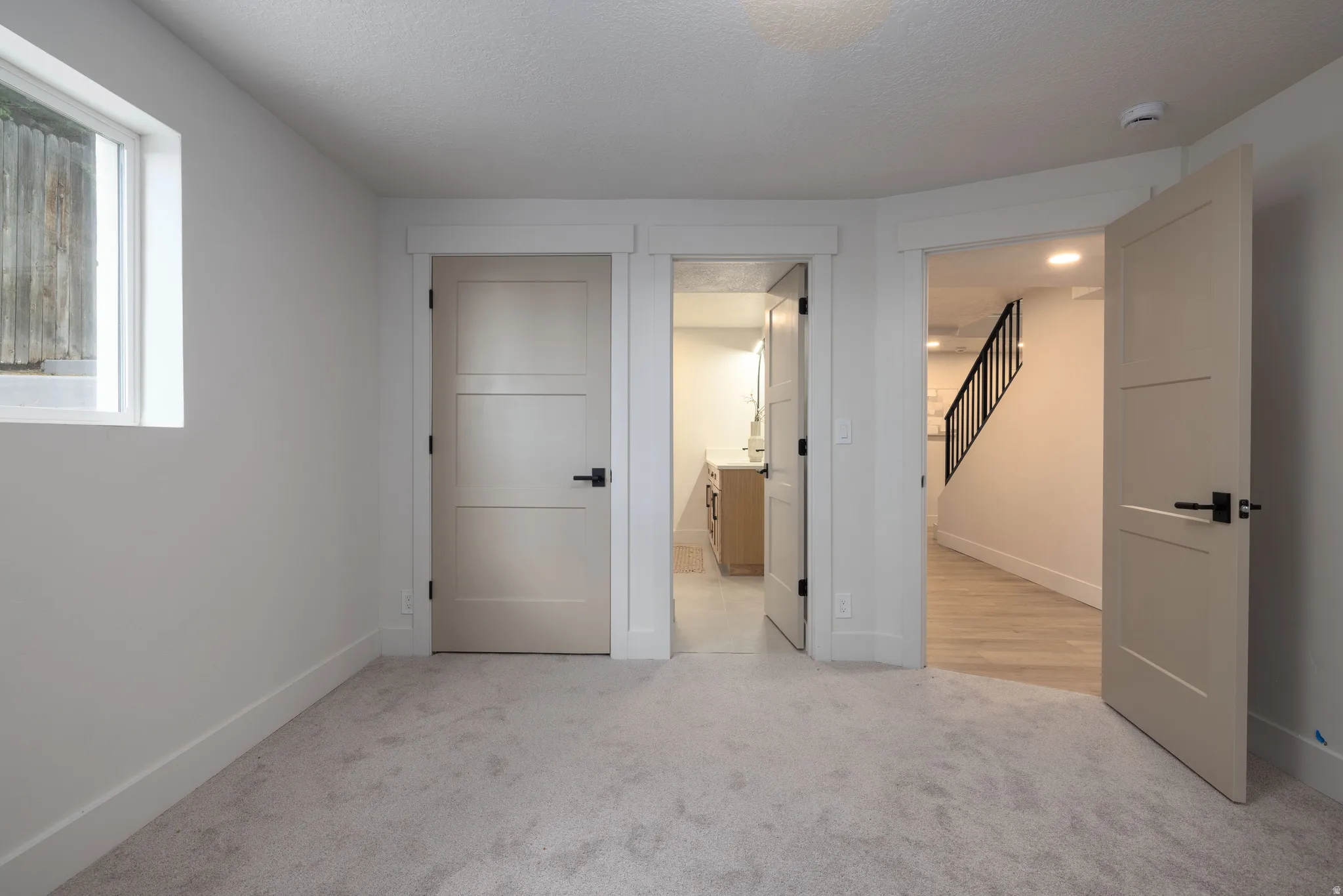 Carpeted room featuring a single window and multiple doors with modern black hardware