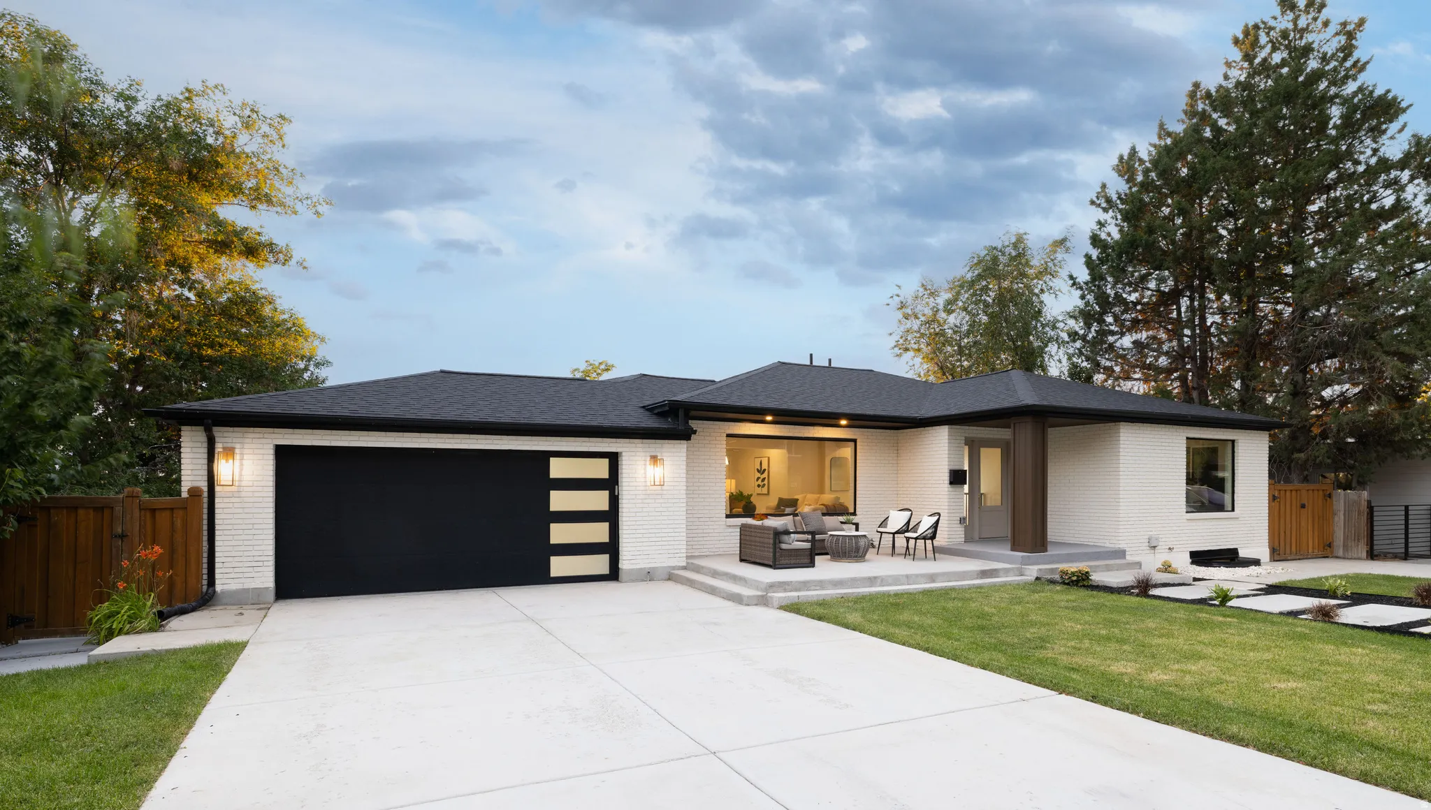 Contemporary ranch-style residence featuring a white brick exterior, a black shingle roof, and a large concrete driveway