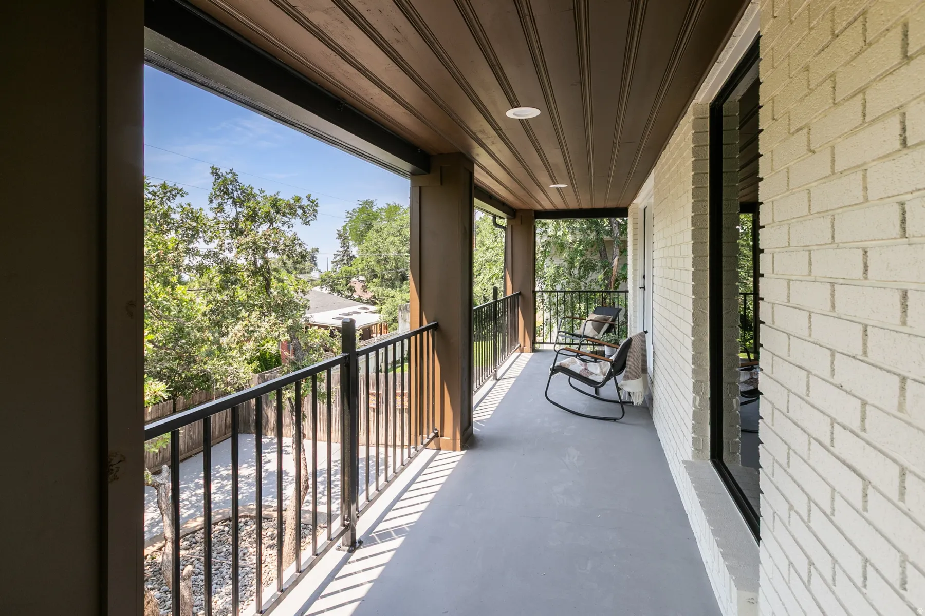 Covered outdoor balcony featuring white brick siding, dark wood-finish ceiling, recessed lighting, and black metal railings