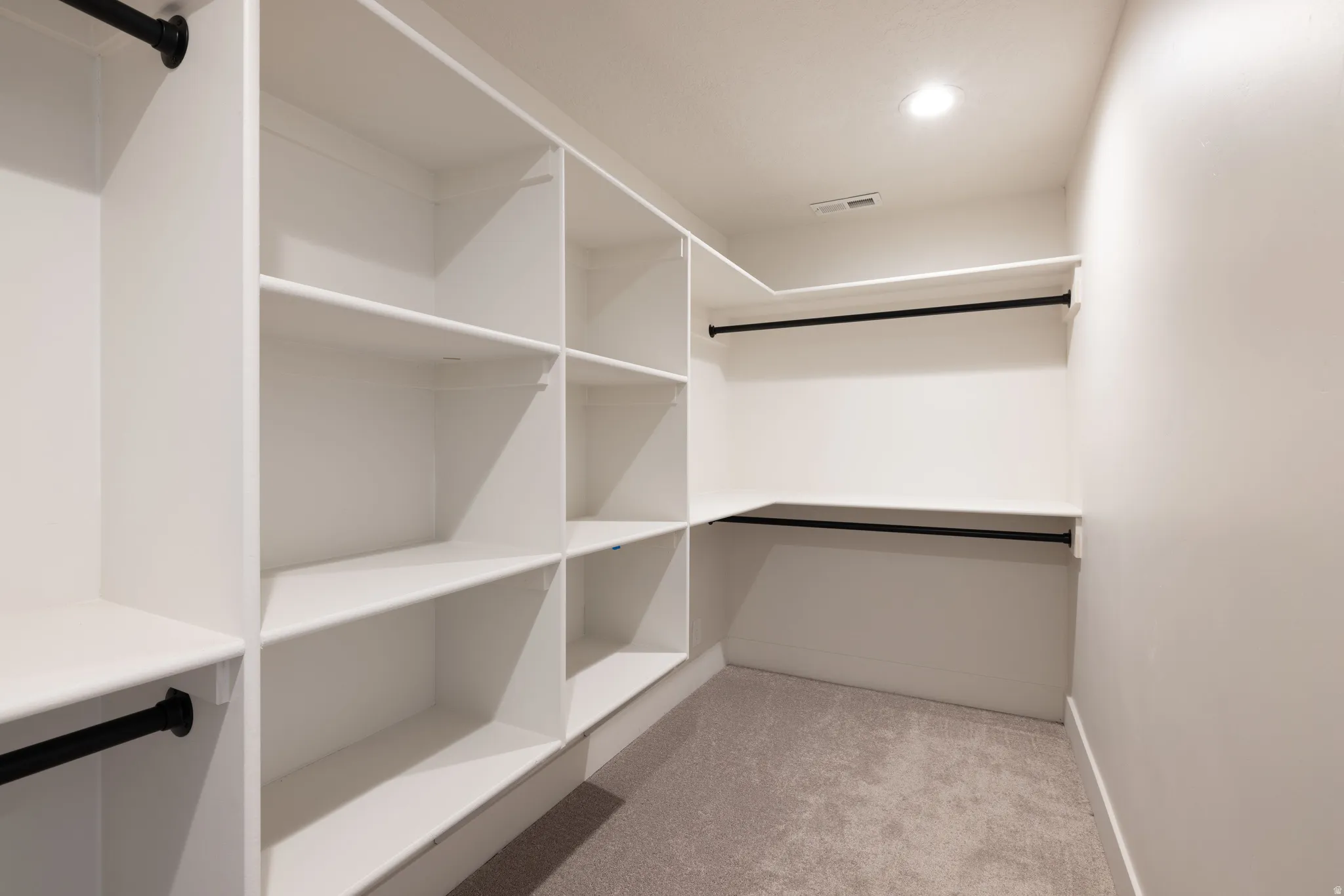 Walk-in closet featuring built-in shelving, multiple hanging rods, recessed lighting, and carpet flooring