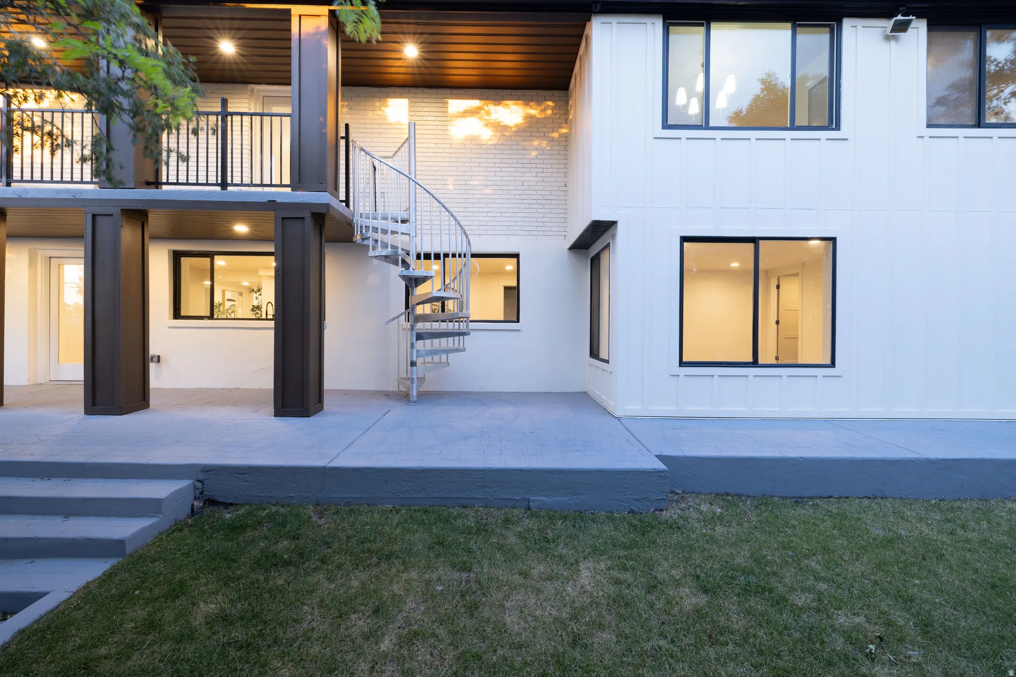 Exterior showcasing a white spiral staircase, upper-level balcony with dark railings, and a concrete patio