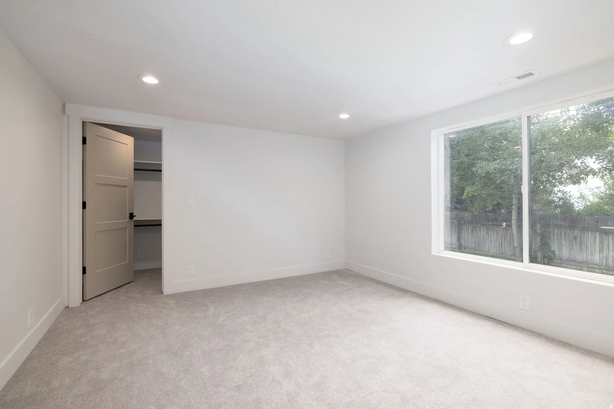 Carpeted room with recessed lighting and a large window featuring a tree-lined exterior