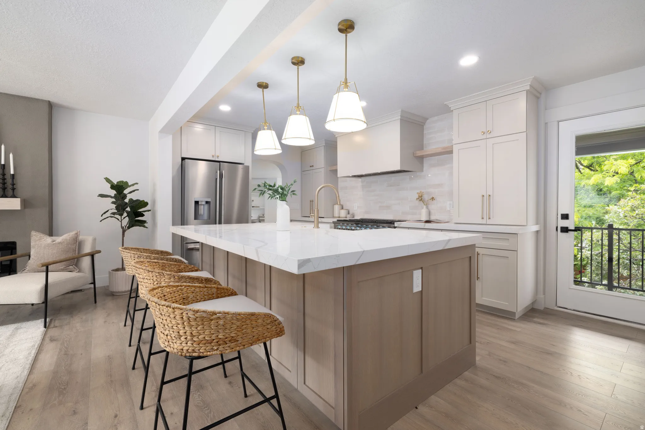 Spacious kitchen featuring a large central island with a light-toned wood-finish base and a light countertop, stainless steel appliances, white cabinetry, and a glass-paned door opening to an exterior balcony