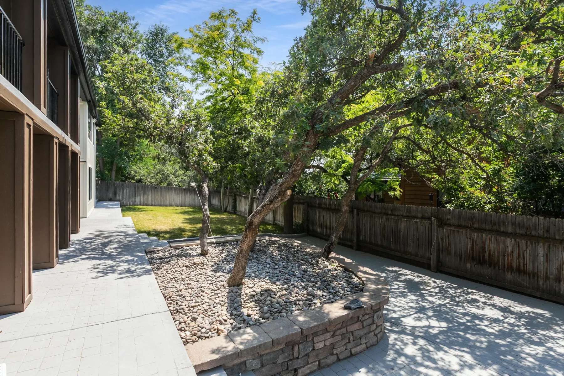 Paved patio area featuring a stone-clad retaining wall and two mature trees