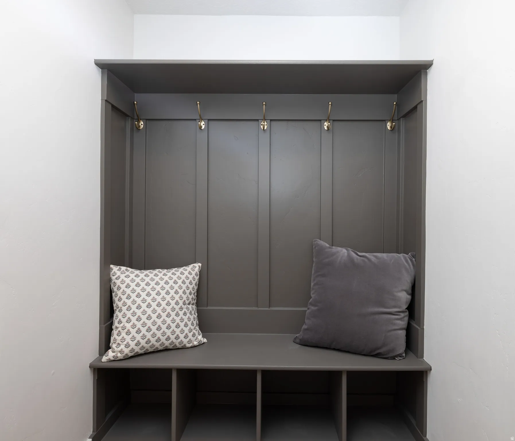 Built-in mudroom bench featuring paneled backing, four brass-finish hooks, and four lower cubbies