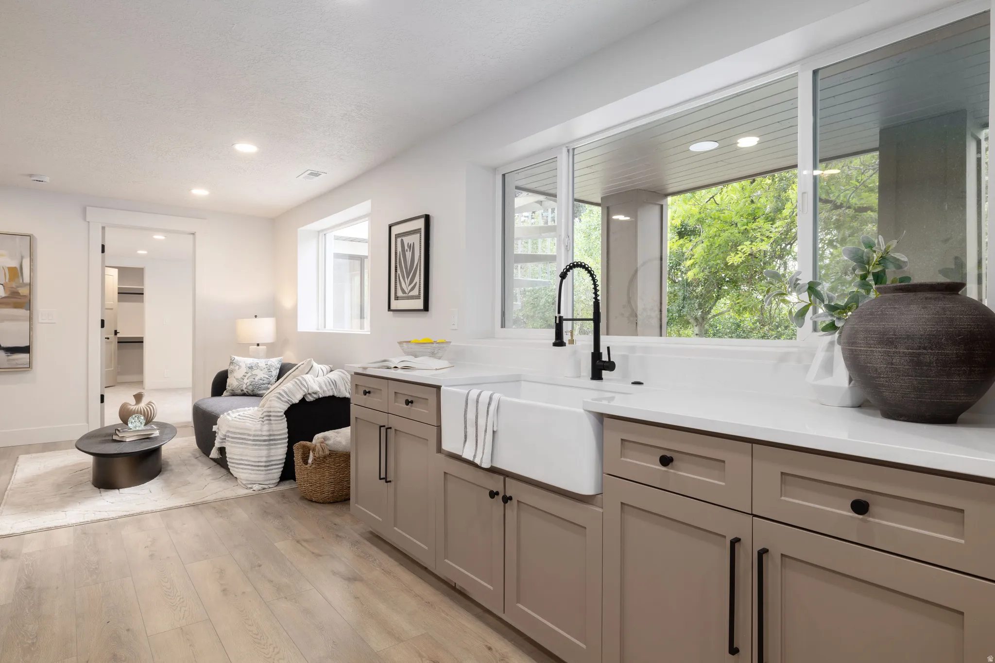 Kitchenette featuring a white farmhouse sink, matte black faucet, and light-toned cabinetry with dark hardware