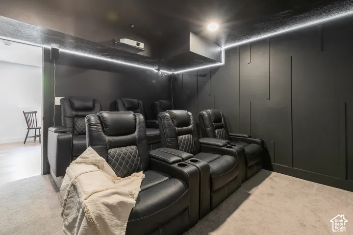 Dedicated media room with dark walls and ceiling, wall-mounted projector, recessed lighting, and perimeter strip lighting