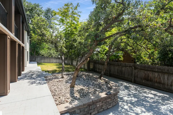Paved patio area featuring a stone-clad retaining wall and two mature trees